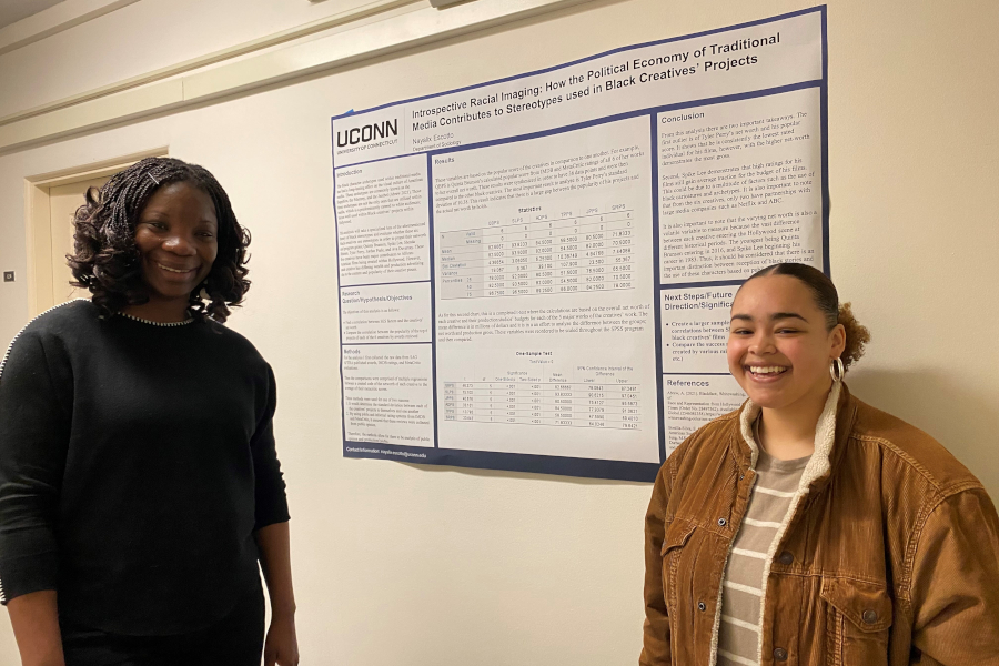 Photo of Nayalix Escotto and faculty advisor Dr. Fumilayo Showers. Behind them is a poster that reads "Introspective Racial Imaging: How the Political Economy of Traditional Media Contributes to Stereotypes used in Black Creatives' Projects"