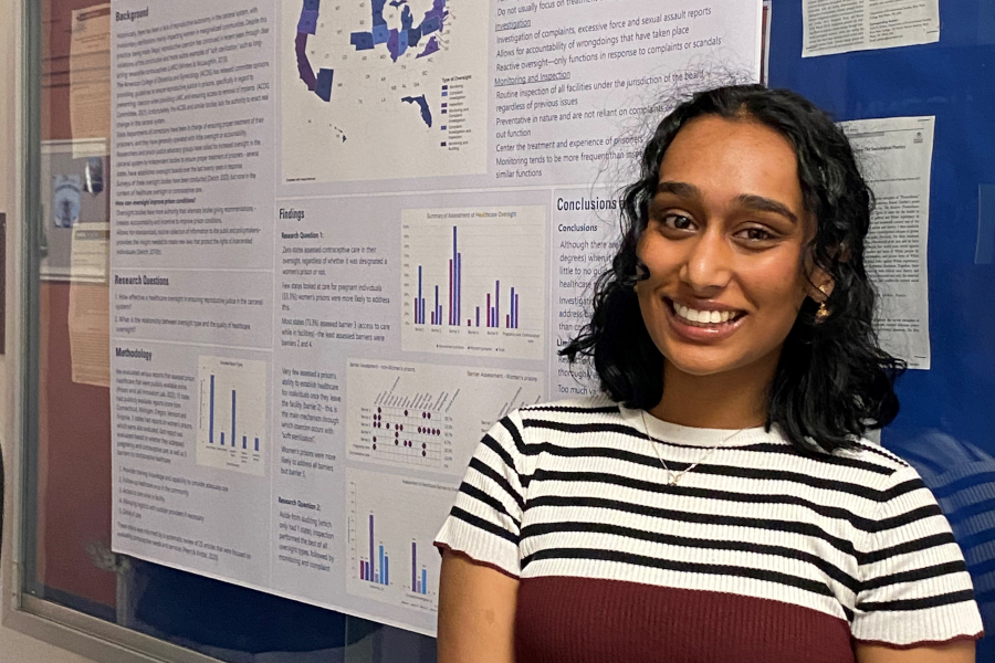 Akshara Iyer stands in front of a research poster. The title, cropped, reads "Ensuring Reproductive Justice in the Carceral System - Evaluation of State Prison Healthcare Oversight"