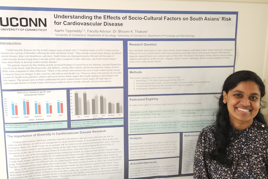 Aarthi Tippireddy stands in front of a research poster entitled "Understanding the Effects of Socio-Cultural Factors on South Asians' Risk for Cardiovascular Disease"