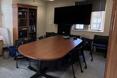 Library with small conference table, chairs, and a wall-mounted TV.