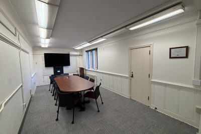 Photo of a conference room containing a table, rolling chairs, and a TV screen.